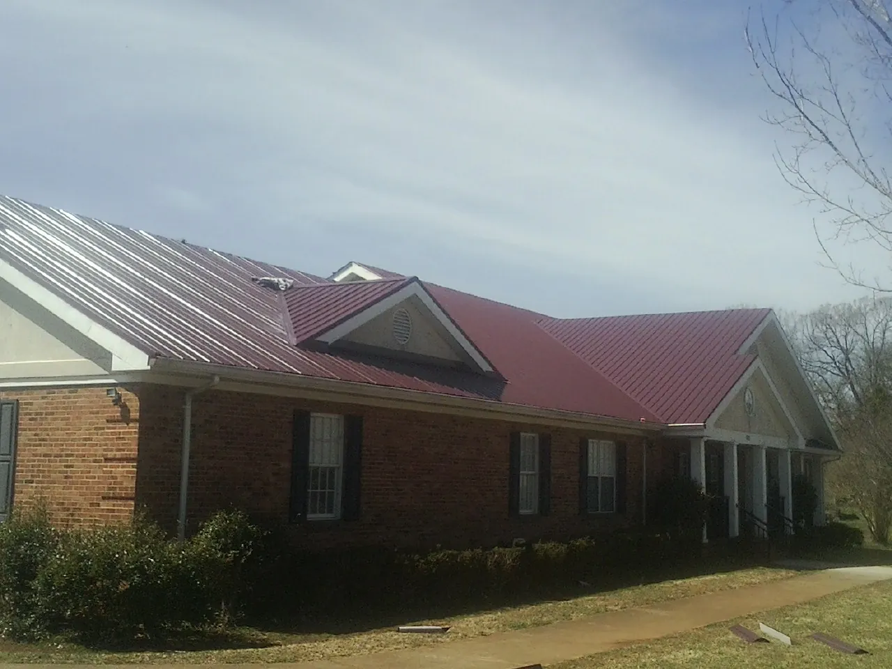 Red metal roof with gabled entries on a long brick building, from a Hail Damage Roof Repair job in Hawaiian Gardens