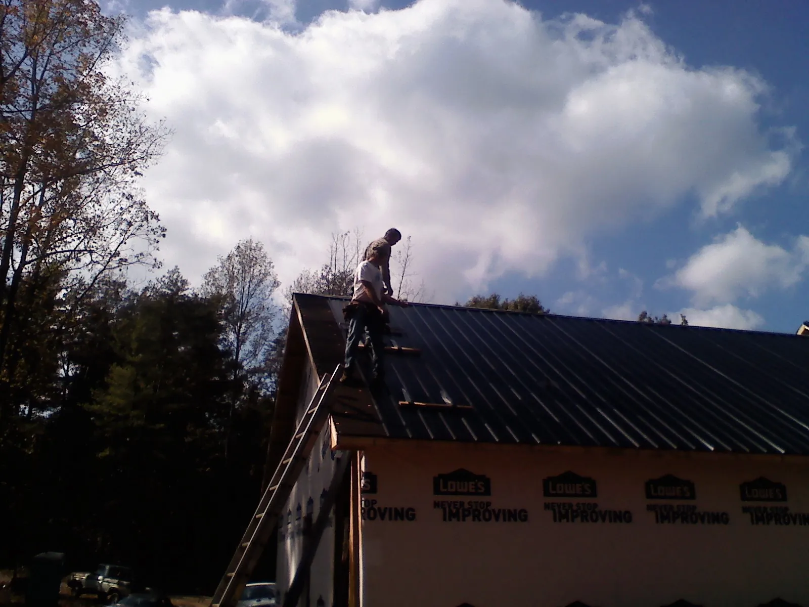 Roofer fastening dark metal panels high against a cloudy sky, from a Roof Inspection job in Hawaiian Gardens