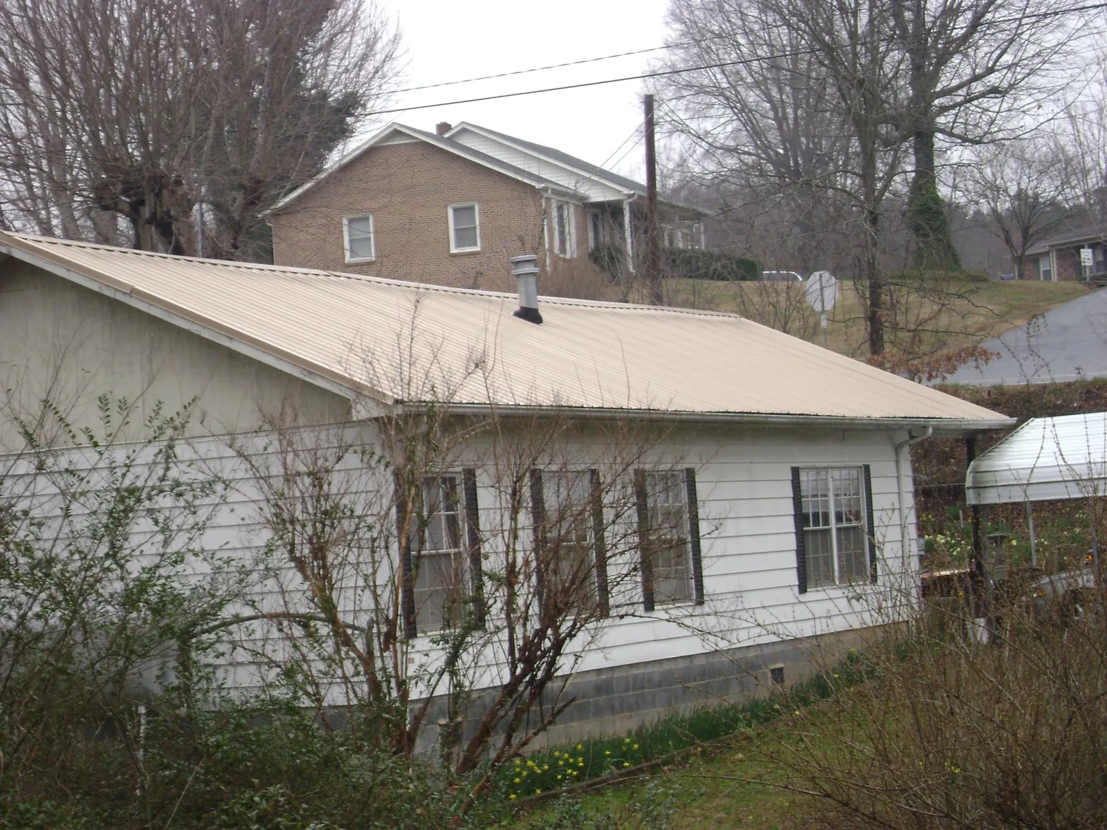 Tan metal roof on a white sided house set into a hillside — Commercial Roofing by Roofing Brothers in Hawaiian Gardens