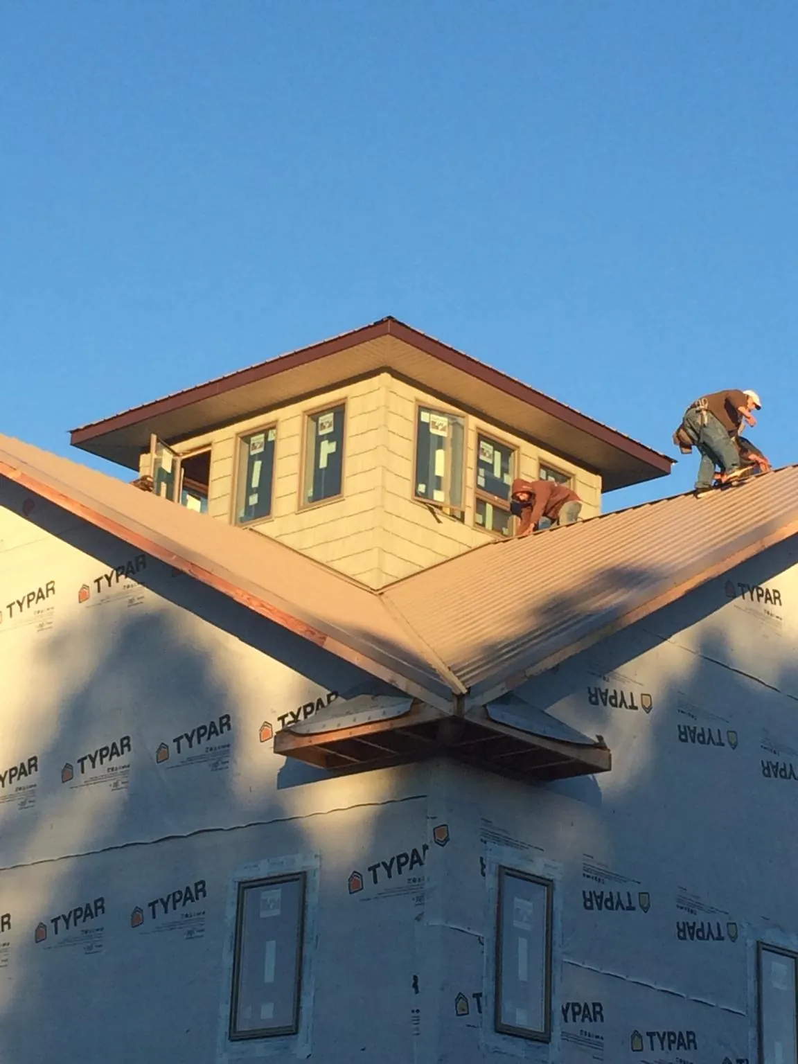 Roofers working around a rooftop cupola on a new metal roof at sunset — Roof Waterproofing in Hawaiian Gardens by Roofing Brothers